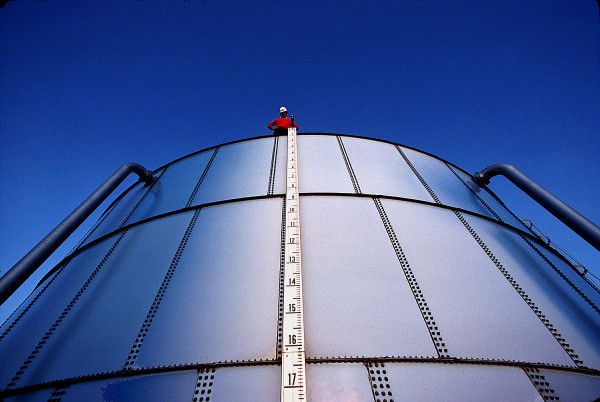 worker on top of oil storage drum with large yard stick